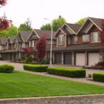 Row of attached townhouses in a Langley BC strata complex with manicured lawn, shaped hedges, and Japanese maples